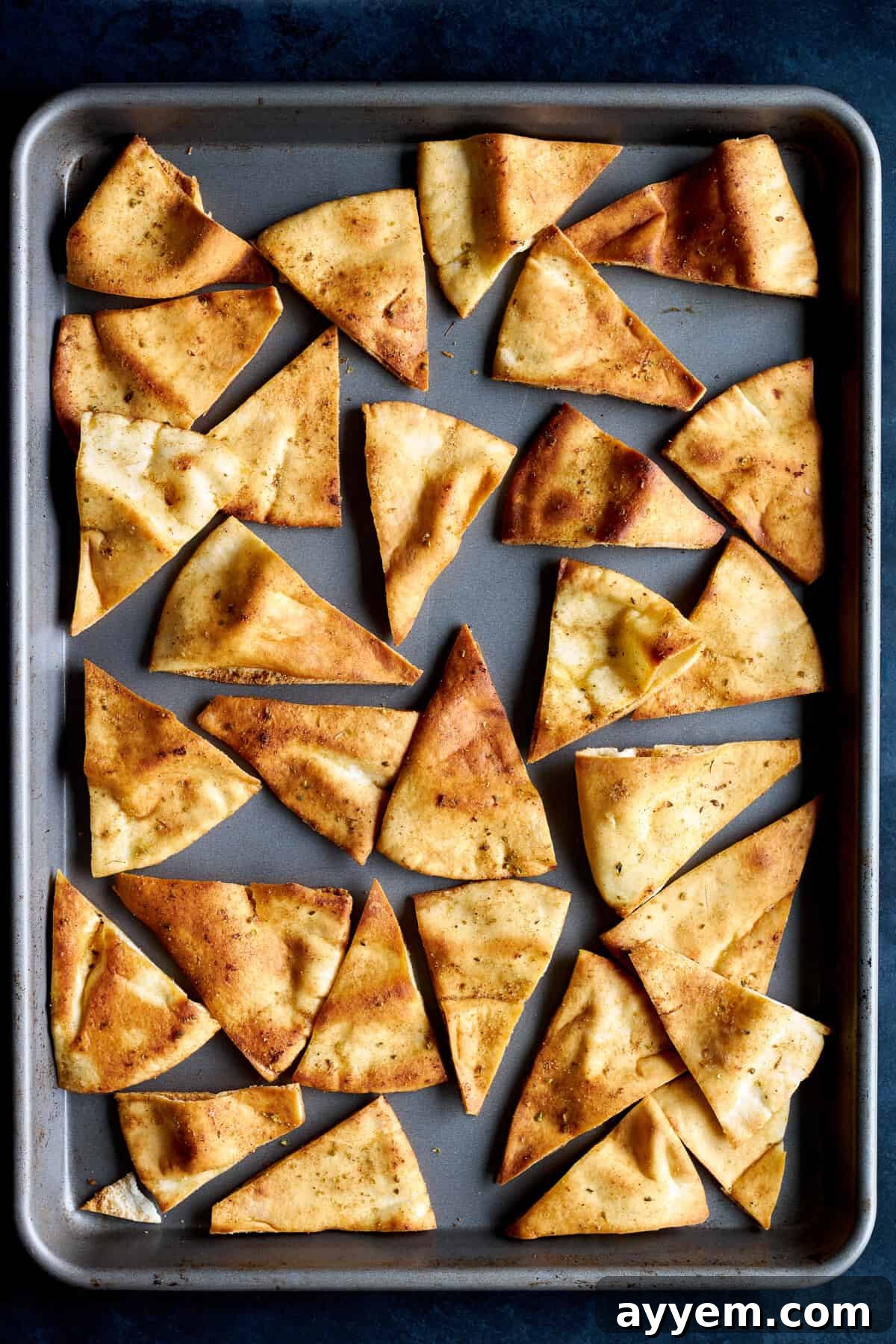A close-up shot of perfectly baked pita chips arranged neatly on a metal baking sheet, showcasing their golden-brown color and inviting texture.
