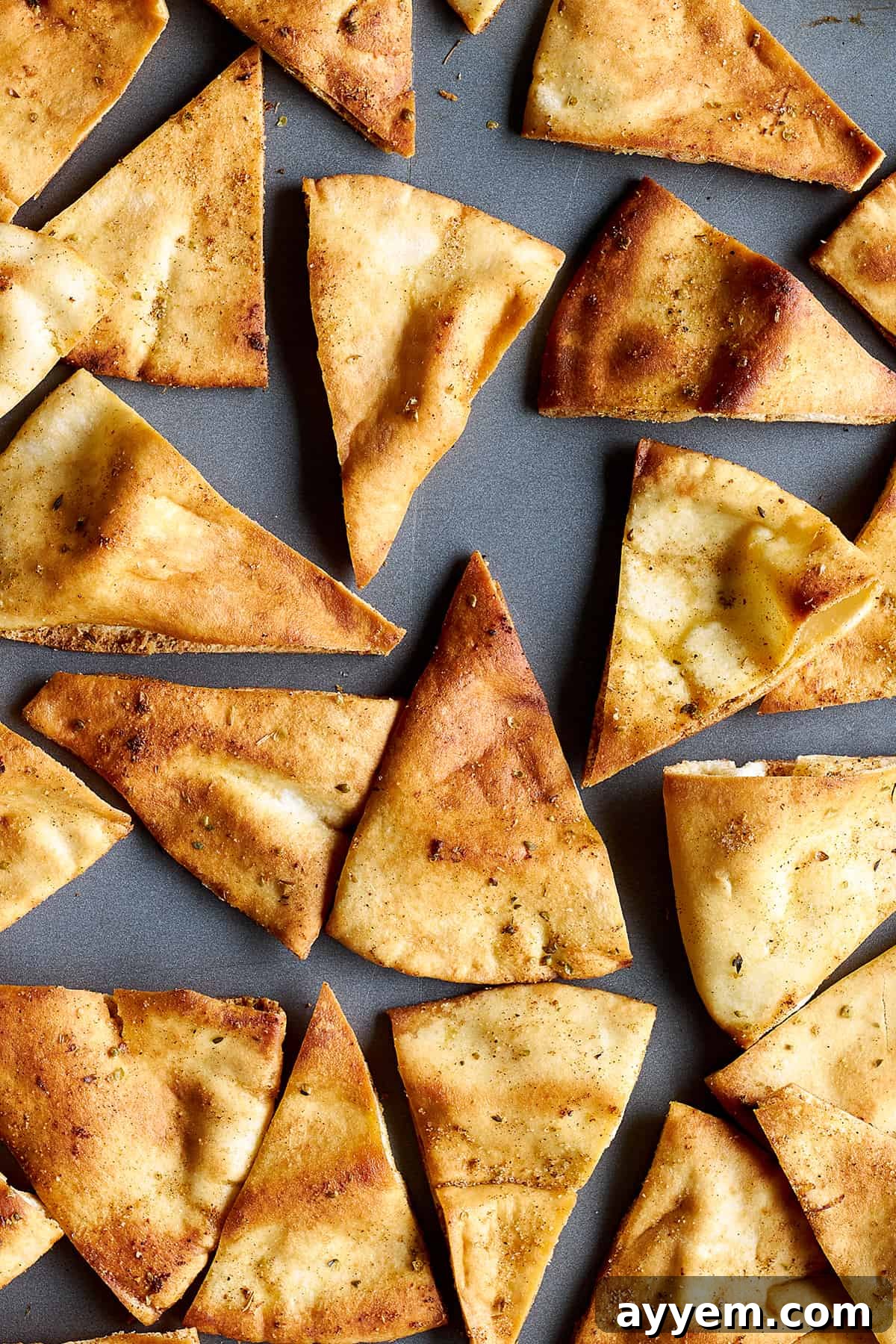 A detailed close-up view of freshly baked, golden-brown pita chips, glistening with seasoning, perfectly arranged on a baking sheet, ready to be enjoyed.