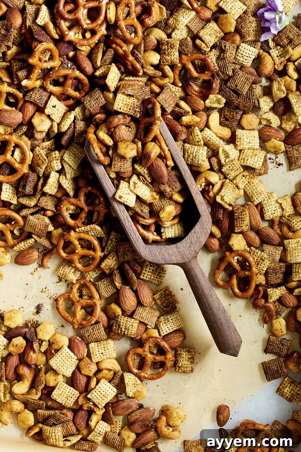 A wooden scoop lifting a generous portion of freshly baked Middle Eastern Spicy Chex Mix from a parchment-lined baking sheet.