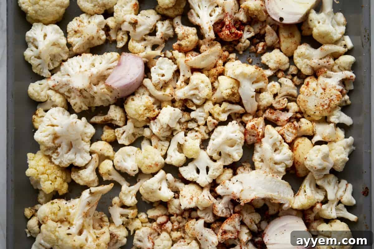Seasoned cauliflower, shallots, and onions on a baking sheet. 