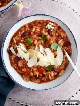 A comforting bowl of Slow Cooker Pasta and Beans Soup (Pasta E Fagioli) garnished with freshly grated Parmesan cheese and fresh herbs, perfect for a cozy meal.