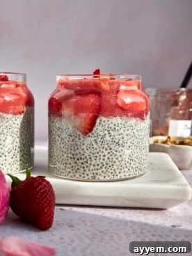 A vibrant side view of a beautifully layered glass jar filled with luscious strawberry chia pudding, generously topped with smooth strawberry puree and fresh strawberry slices.