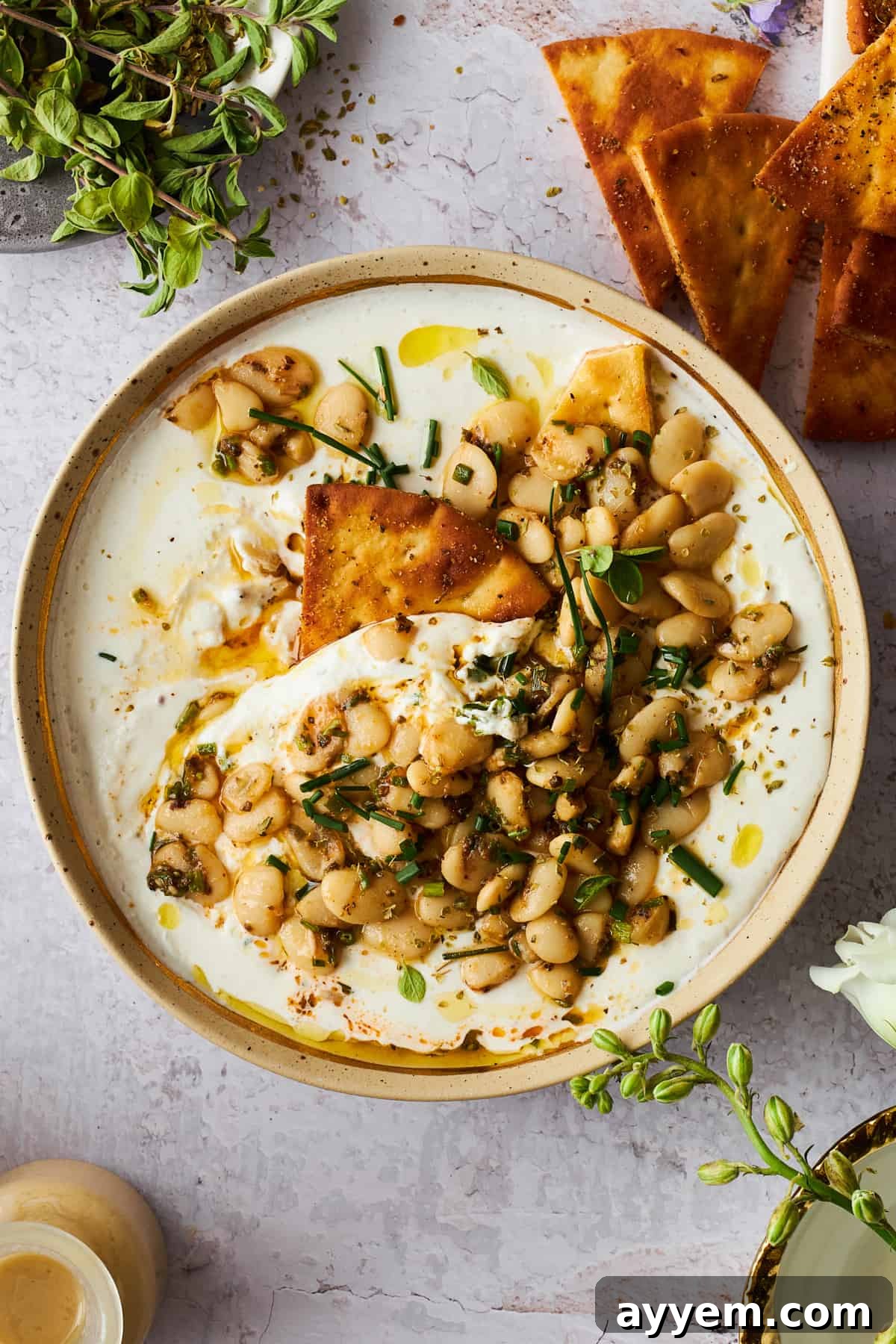 A bowl of marinated butter beans and cottage cheese with a pita chip dipped in. This healthy snack or appetizer features creamy whipped cottage cheese topped with savory, herb-infused butter beans, perfect for dipping.