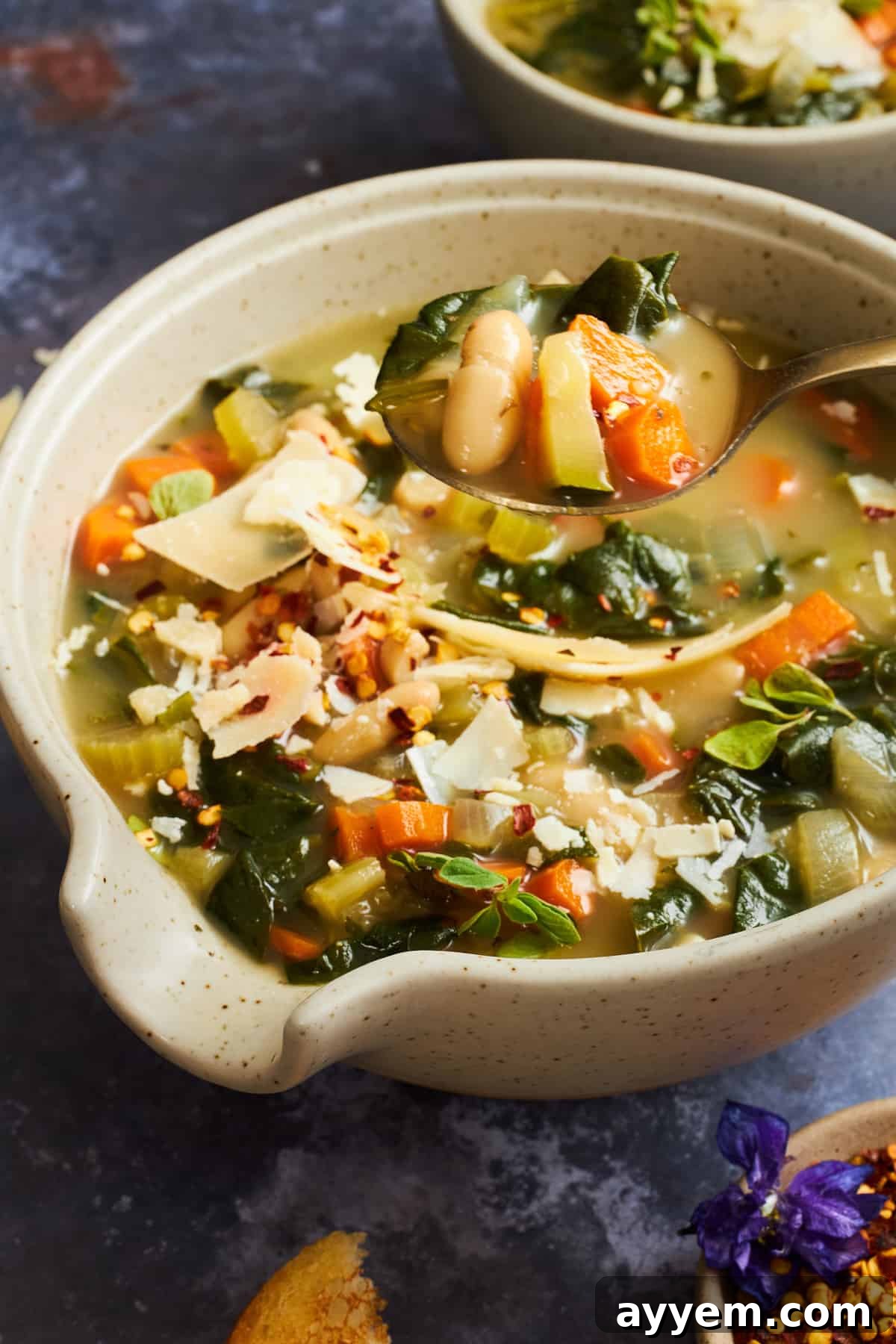 A spoon lifting a bite from a bowl of white bean soup. 