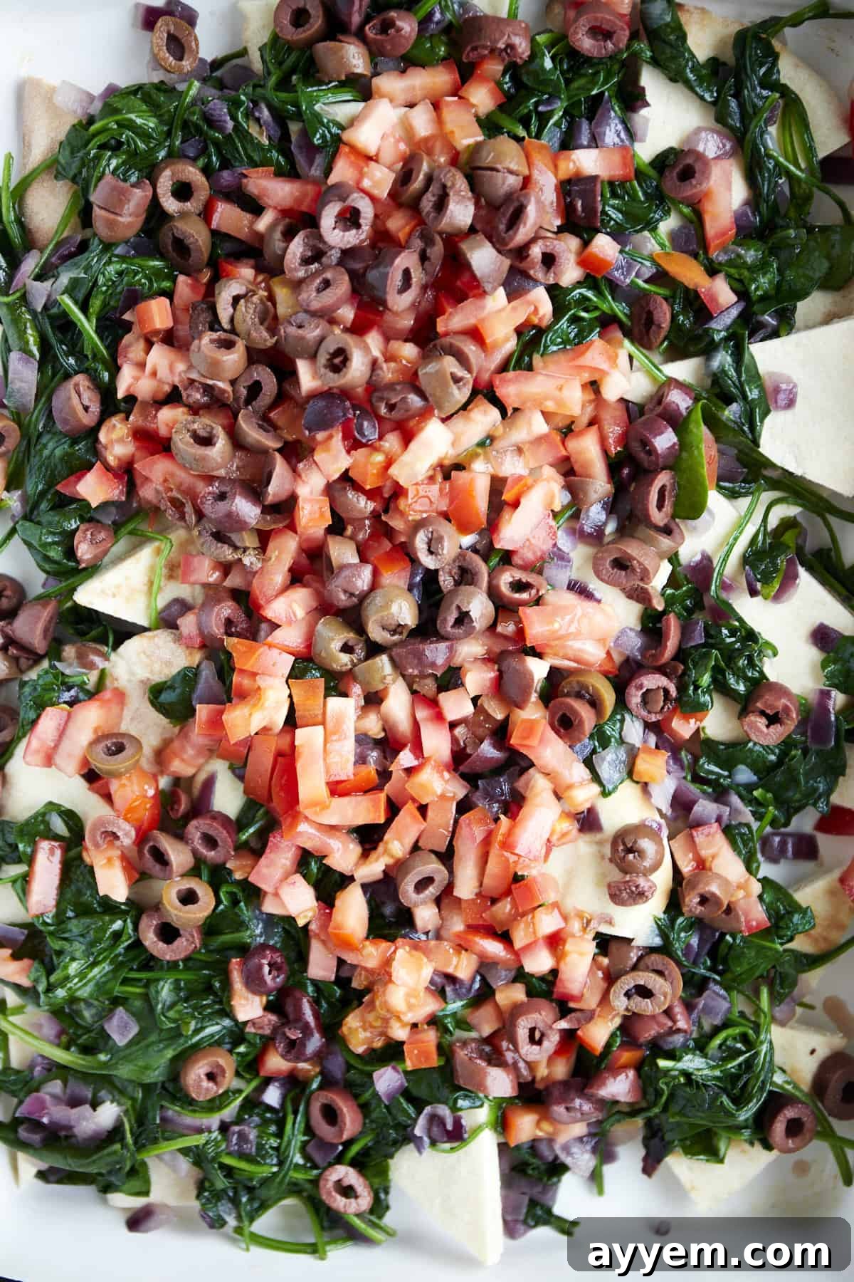 A layer of perfectly sautéed red onions, spinach, and tomatoes spread over pita bread in a casserole dish.