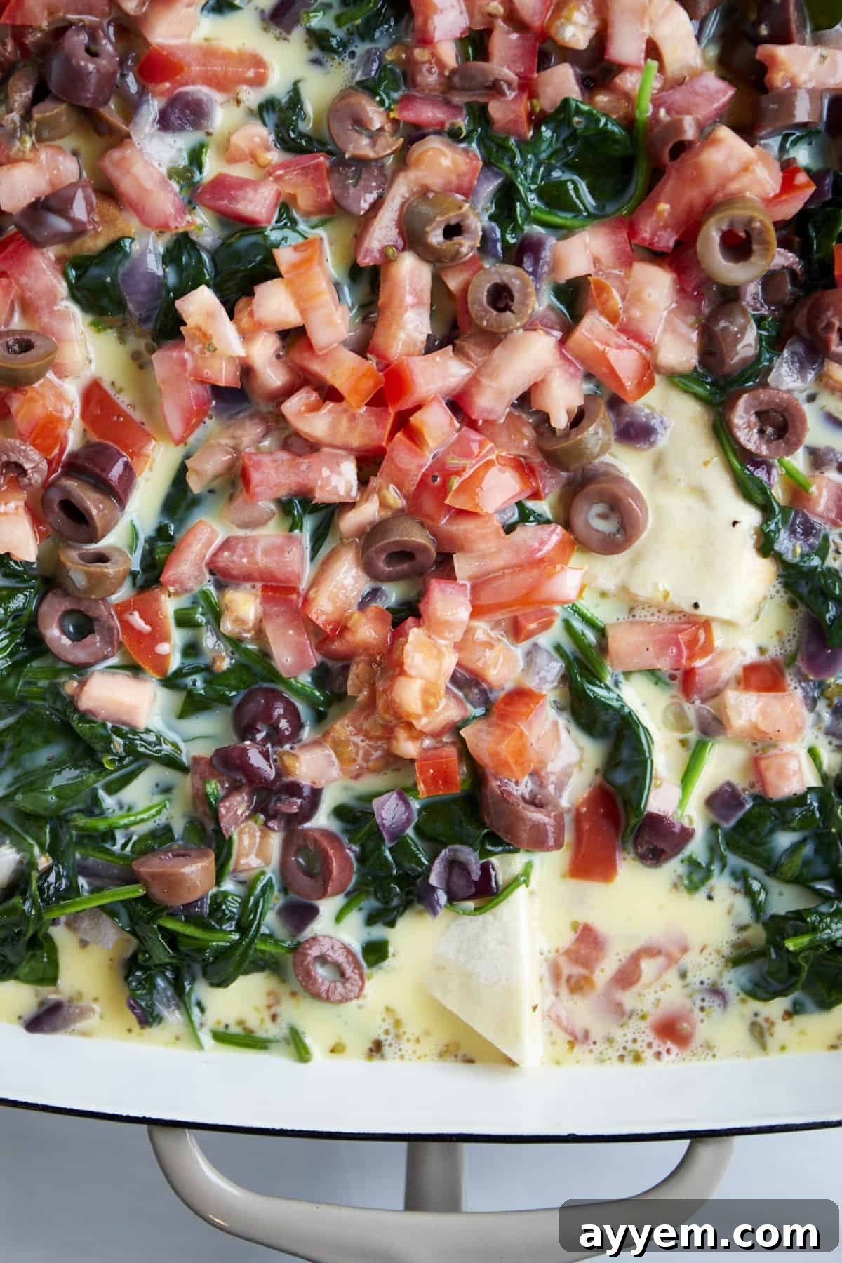 Whisked eggs and milk being poured over the vegetable and pita layers in a baking dish, preparing for baking.