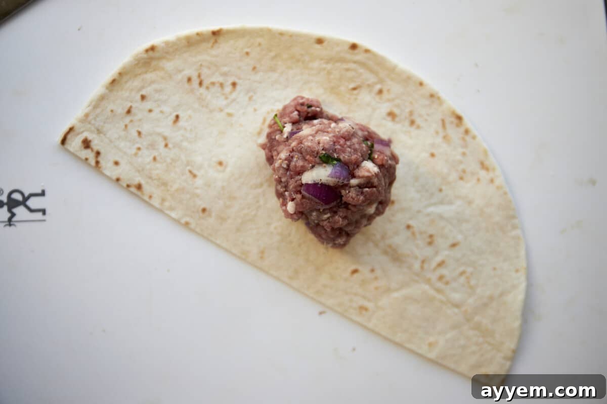Raw ground beef in the center of a tortilla half.