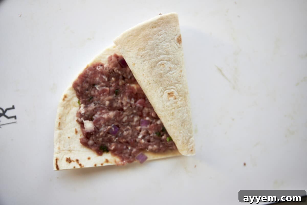 A tortilla being rolled up with ground beef in the center.