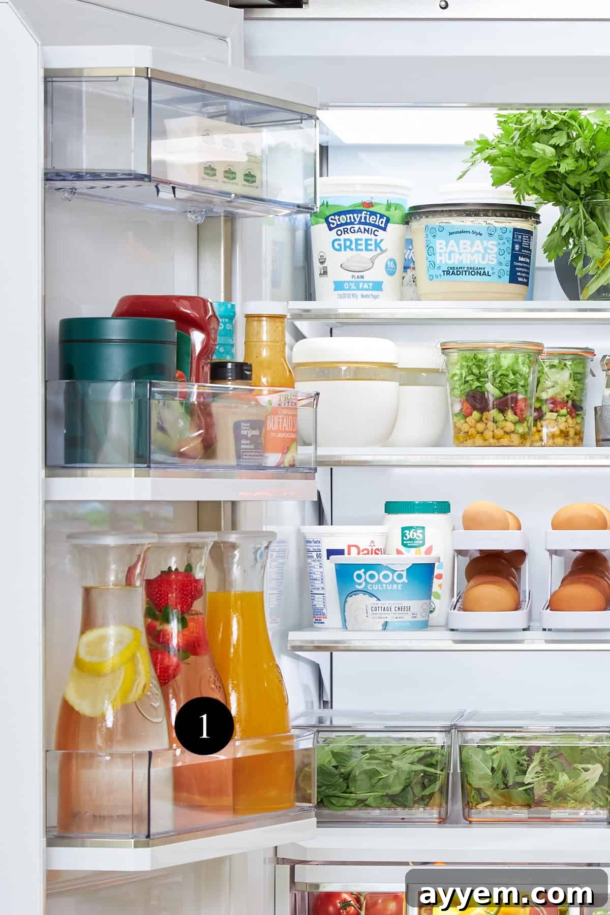 A glass pitcher filled with juice and a jar of pickles with a strainer, both neatly stored in a refrigerator.