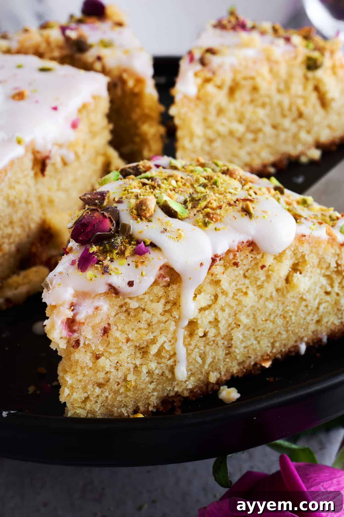 A top-down view of a beautifully decorated Persian love cake, showcasing the intricate patterns of rose petals and pistachios on its glistening orange glaze.