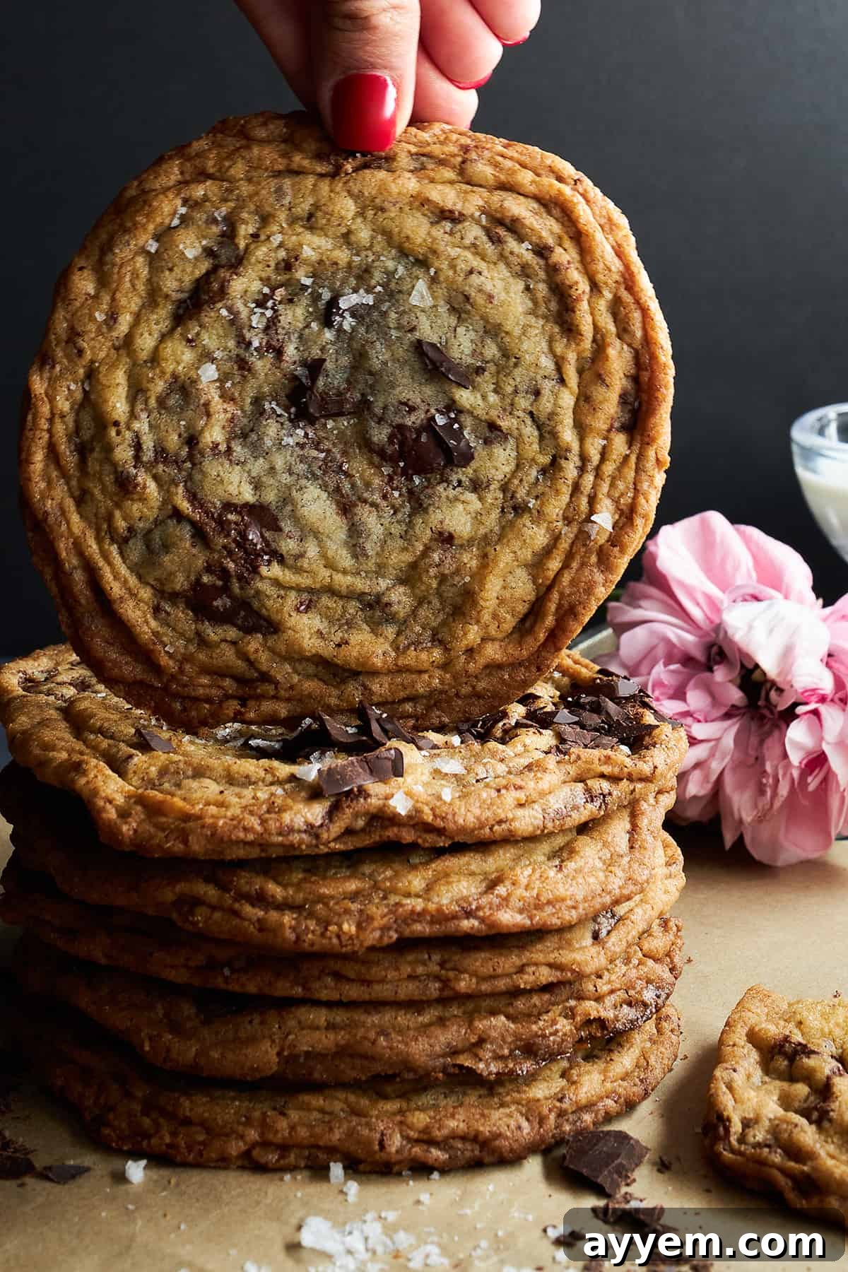 A hand lifting a banging chocolate chip cookie off a stack of cookies.