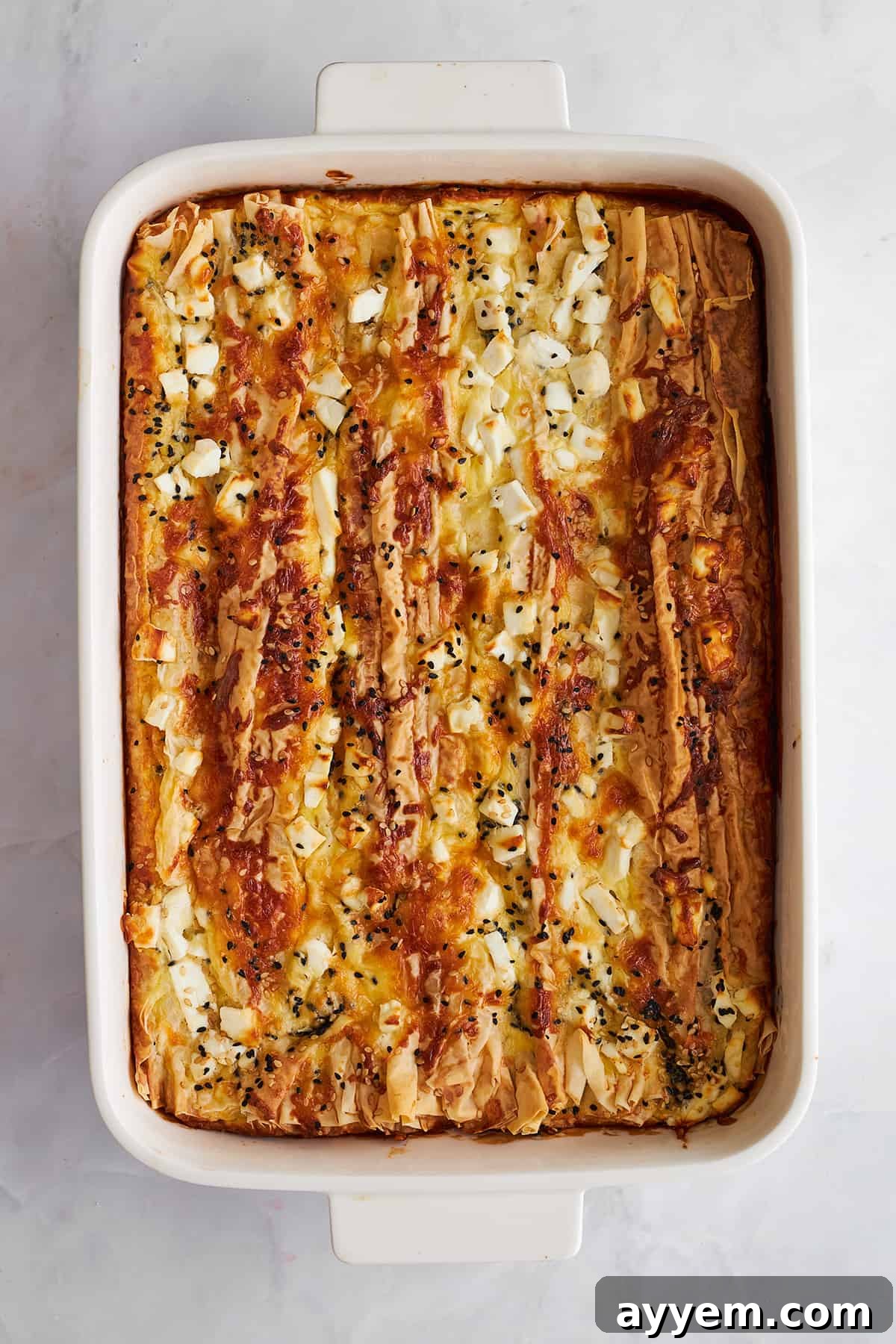 A baking dish filled with golden-brown feta cheese phyllo, ready for slicing.