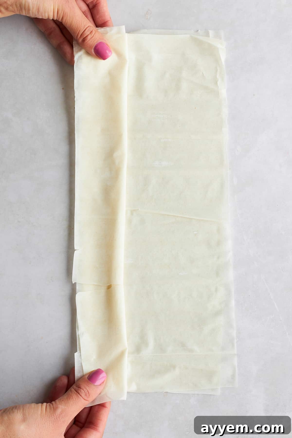A hand gently scrunching a sheet of phyllo dough on a baking surface.