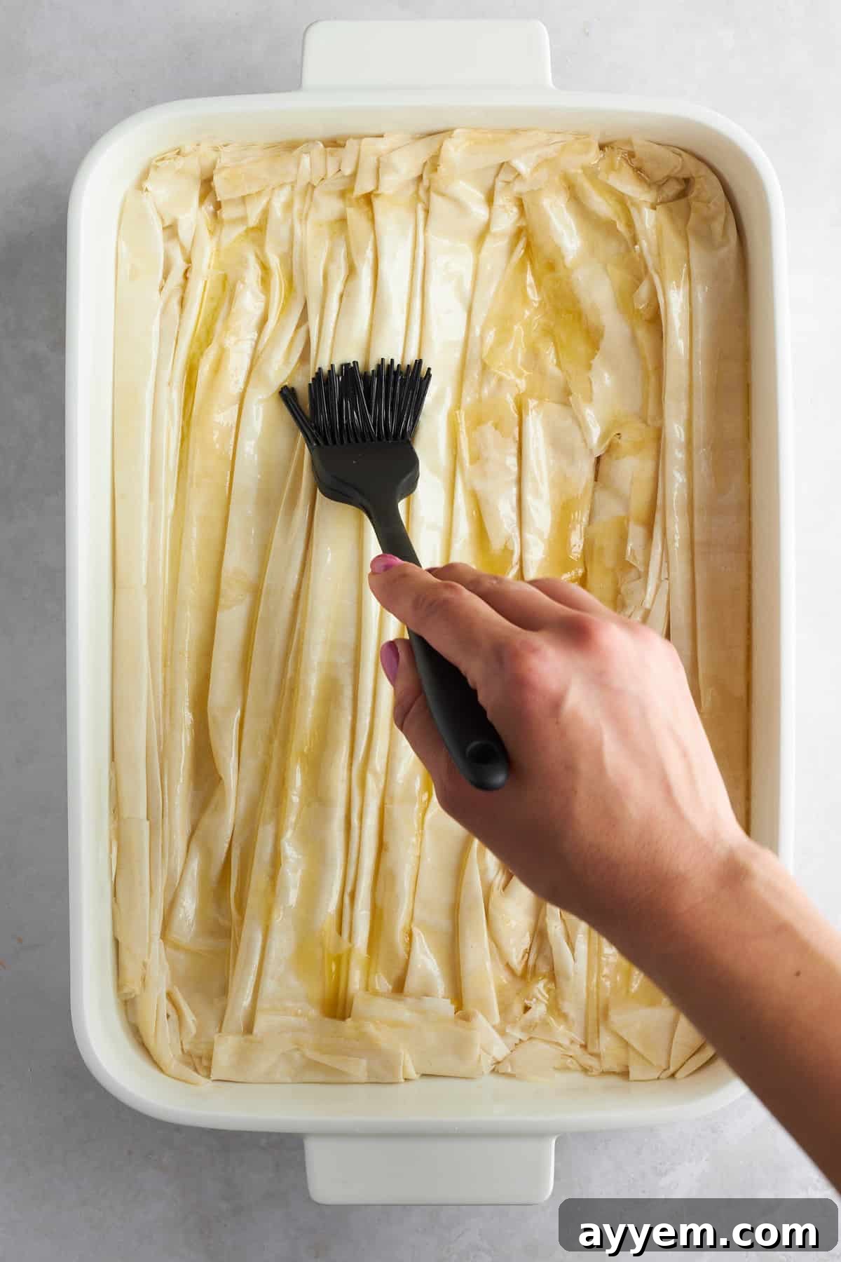 Melted butter being drizzled over partially baked crinkled phyllo dough.