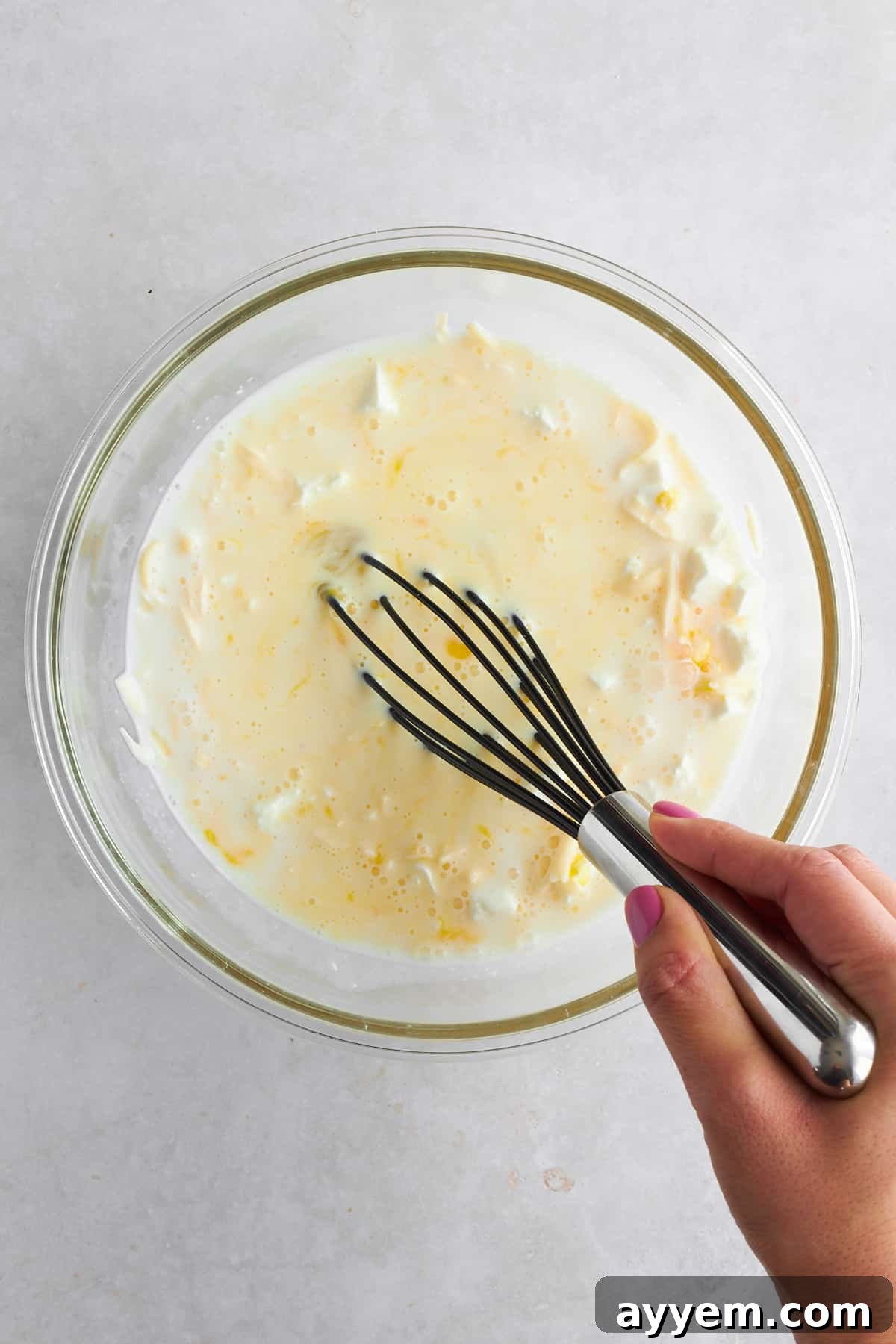 The whisked milk and cheese mixture being poured evenly over the baked phyllo dough in a dish.