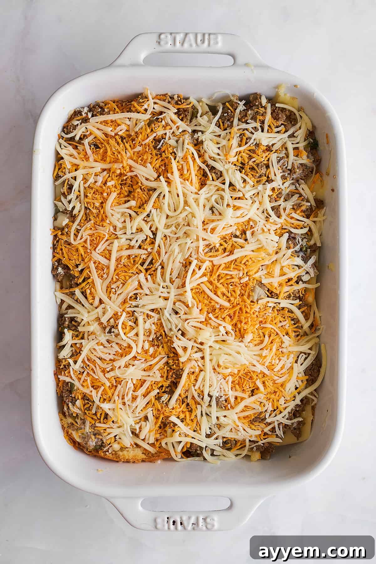 Ground beef sliders being layered in a baking dish. 