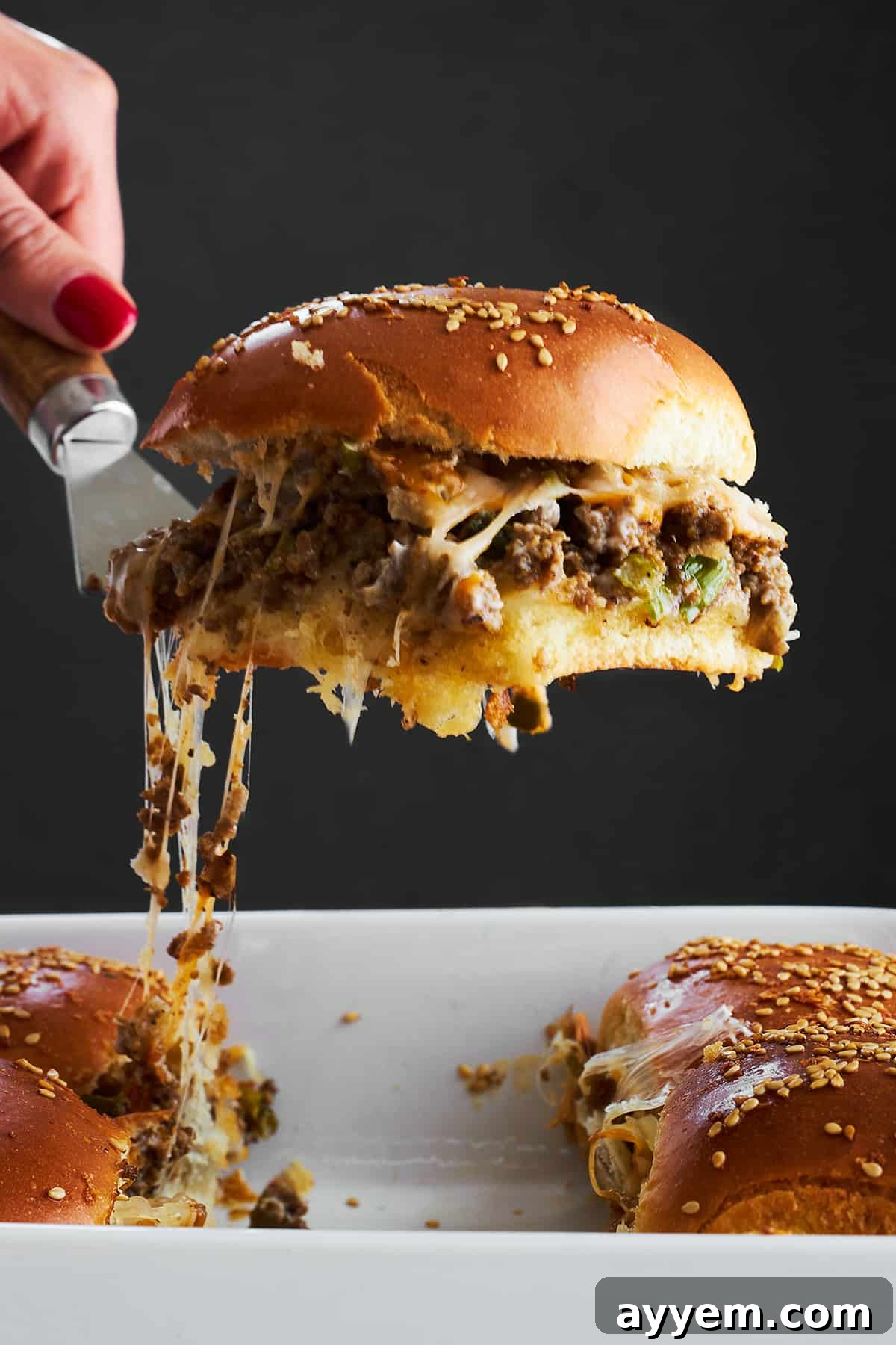 A cheesy ground beef slider being lifted from a baking dish. 