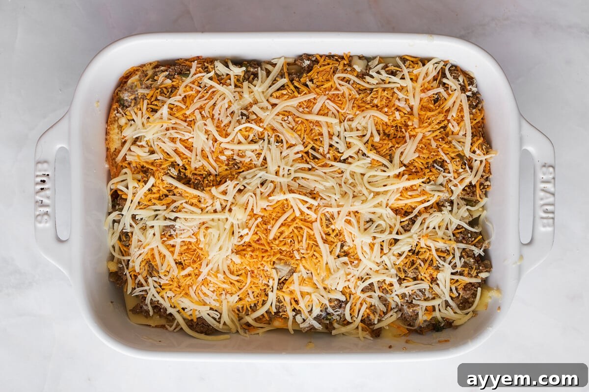 Cheese and beef being layered on slider buns in a baking dish.