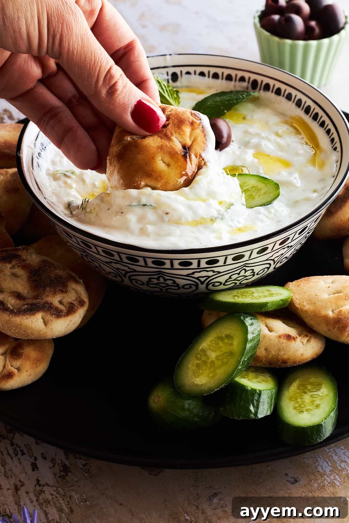 A hand dipping pita bread into a bowl of tzatziki sauce. 