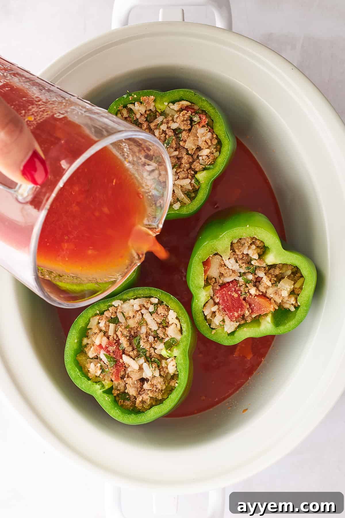 A close-up of tomato sauce being poured from a ladle over stuffed peppers arranged in a slow cooker.