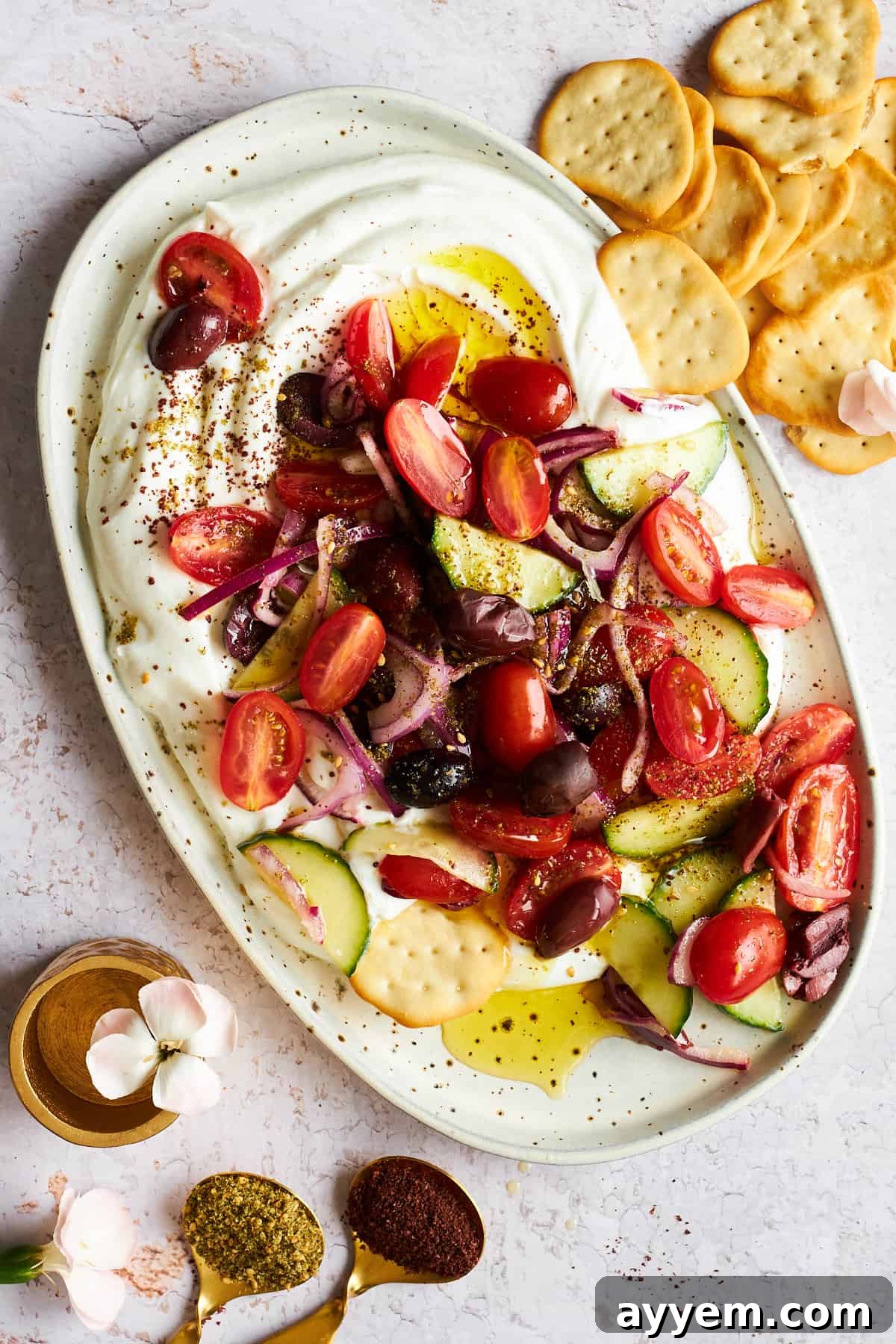 A close-up view of a beautifully arranged Greek salad dip platter, showcasing the distinct layers of smooth yogurt and a colorful medley of chopped Greek salad ingredients, with an assortment of dippers nearby.