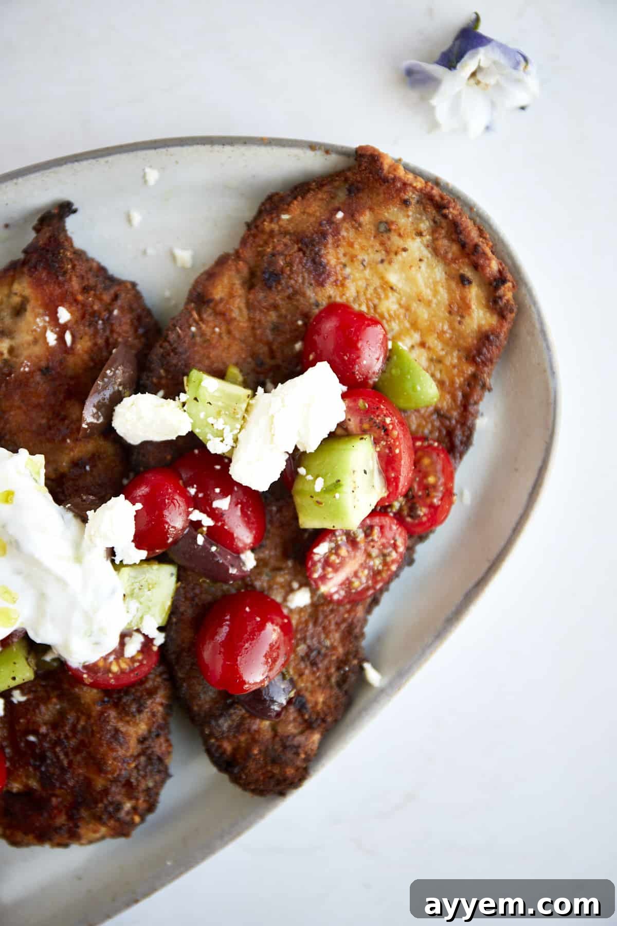 Crispy Air Fryer Chicken Milanese served with a fresh and vibrant Mediterranean salad, garnished with feta cheese and lemon wedges.