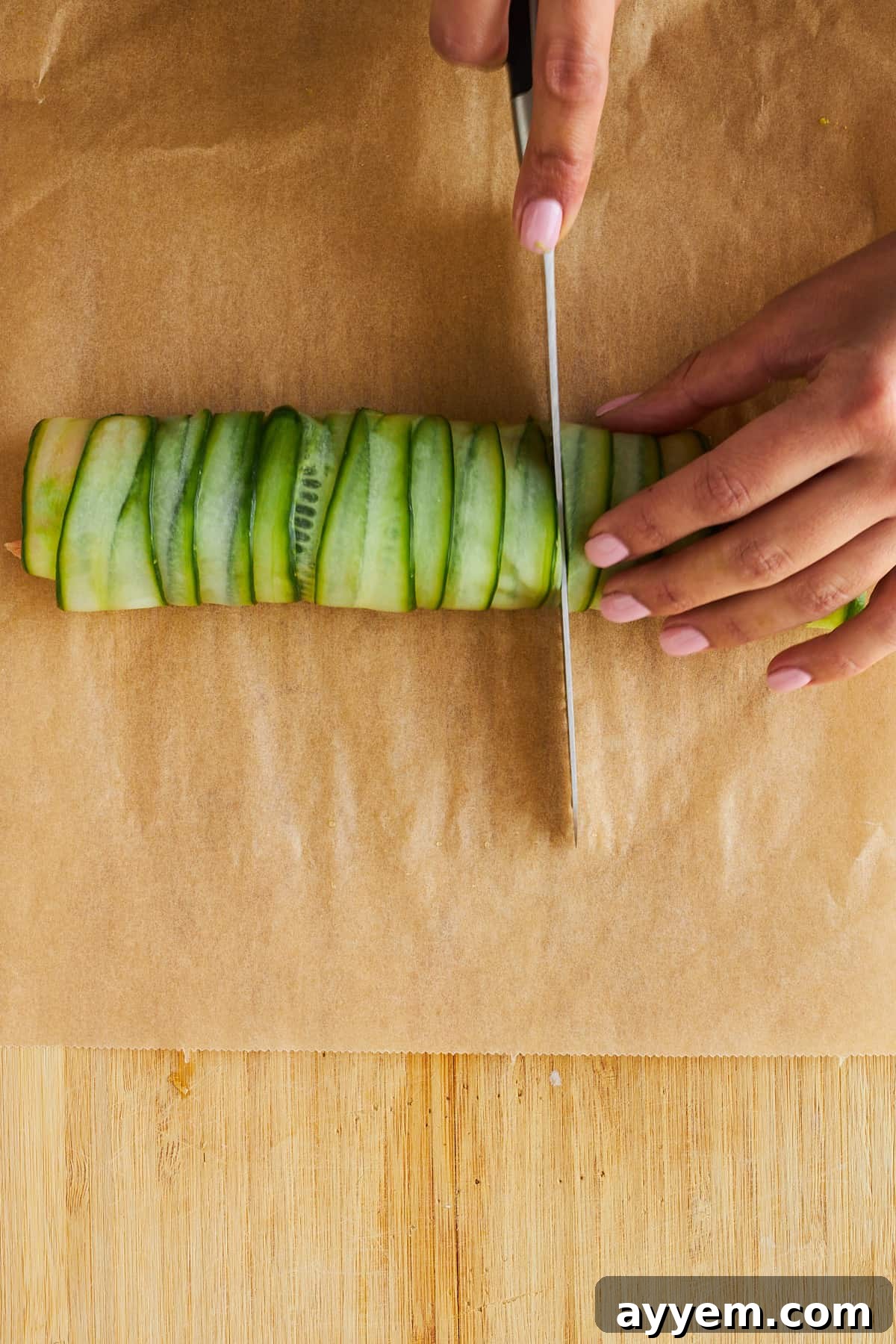 A skilled hand using a sharp knife to slice a long smoked salmon cucumber roll into uniform, bite-sized pieces for serving.