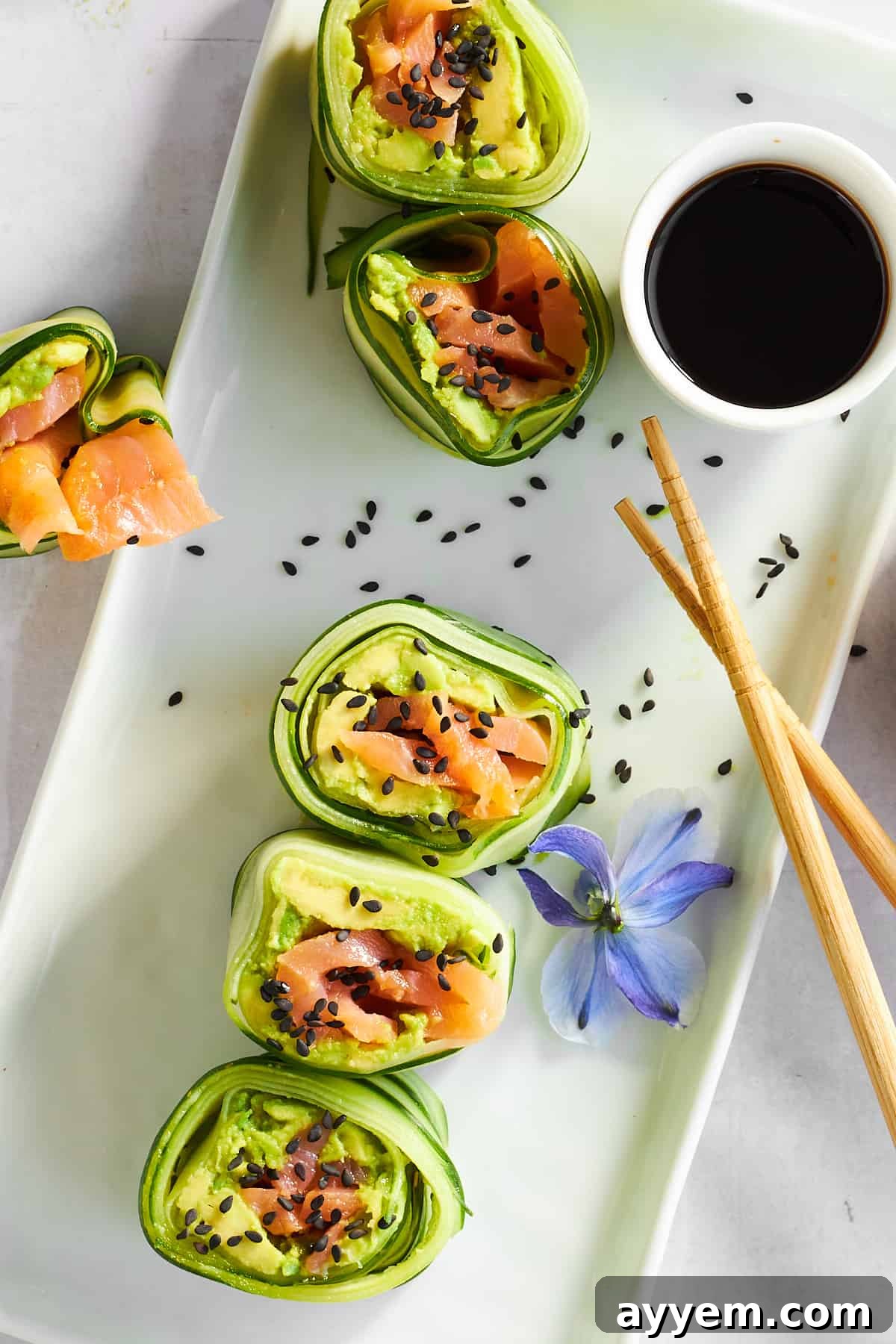 A pristine plate of freshly made smoked salmon cucumber rolls, perfectly arranged and ready to be served alongside a small dish of soy sauce for dipping.