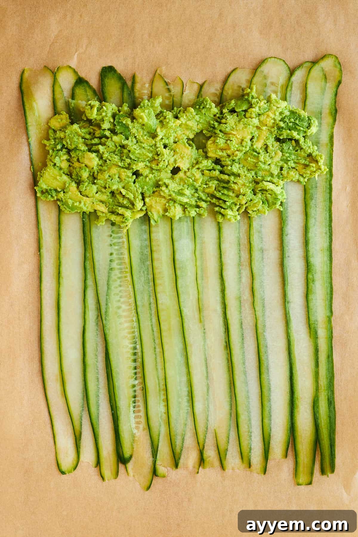 Creamy mashed avocado being spread meticulously over the cucumber strips, near one end, forming the first layer of the filling.