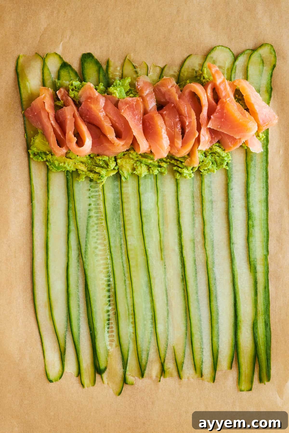 A vibrant layer of smoked salmon strips carefully placed on top of the mashed avocado, resting on the cucumber strips.