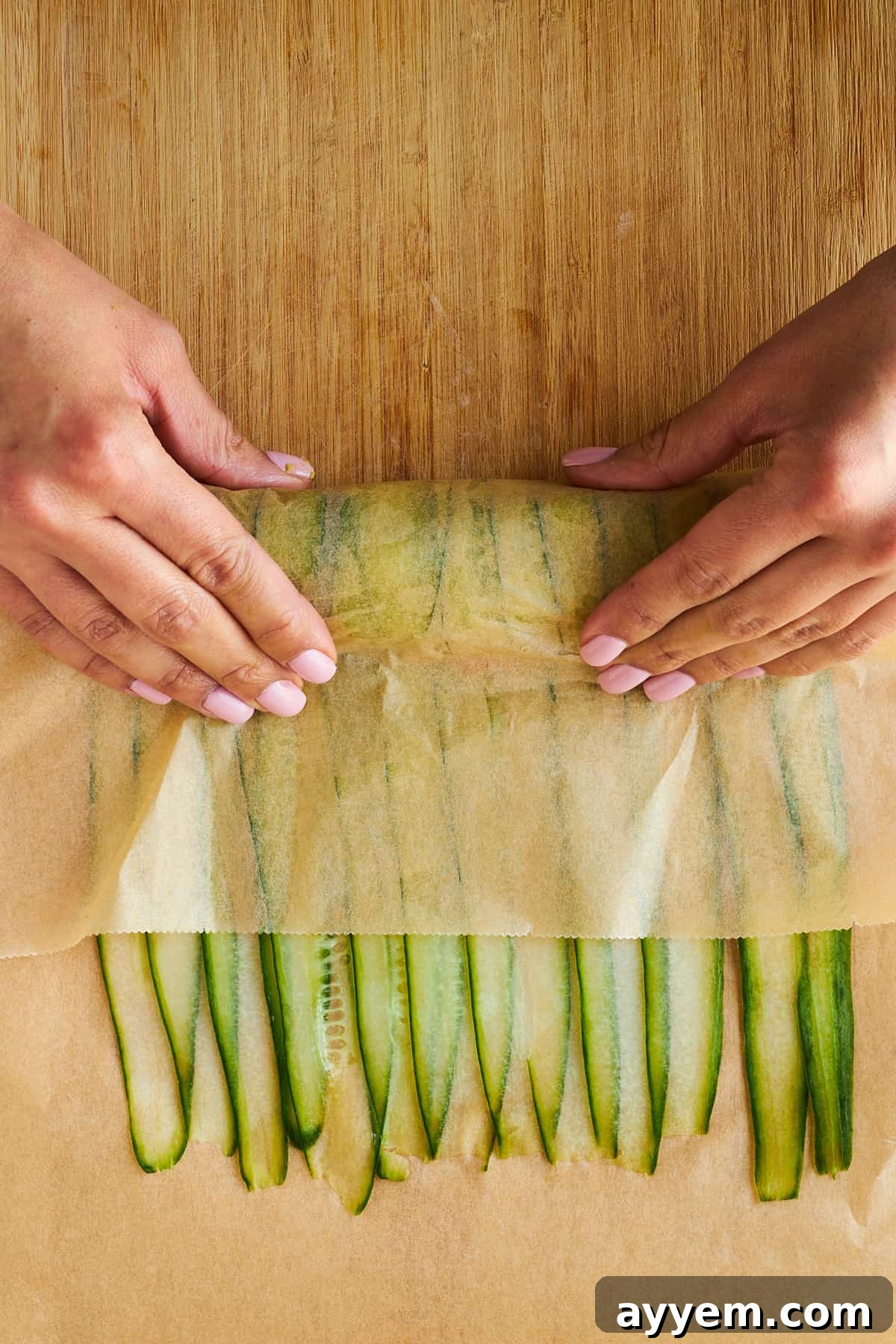 A smoked salmon and avocado filled cucumber roll being gently rolled up from one end, showing the technique for creating a tight wrap.