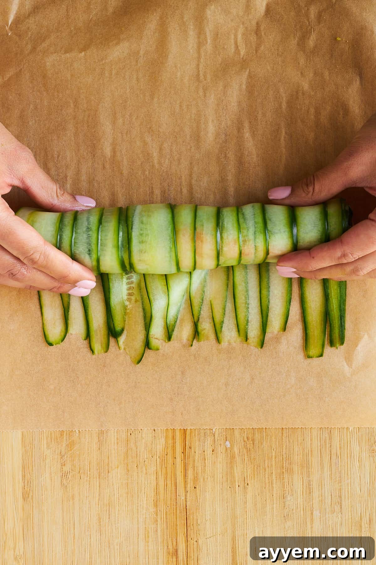 Two hands carefully continuing to roll a cucumber strip, forming a complete and secure smoked salmon cucumber roll.