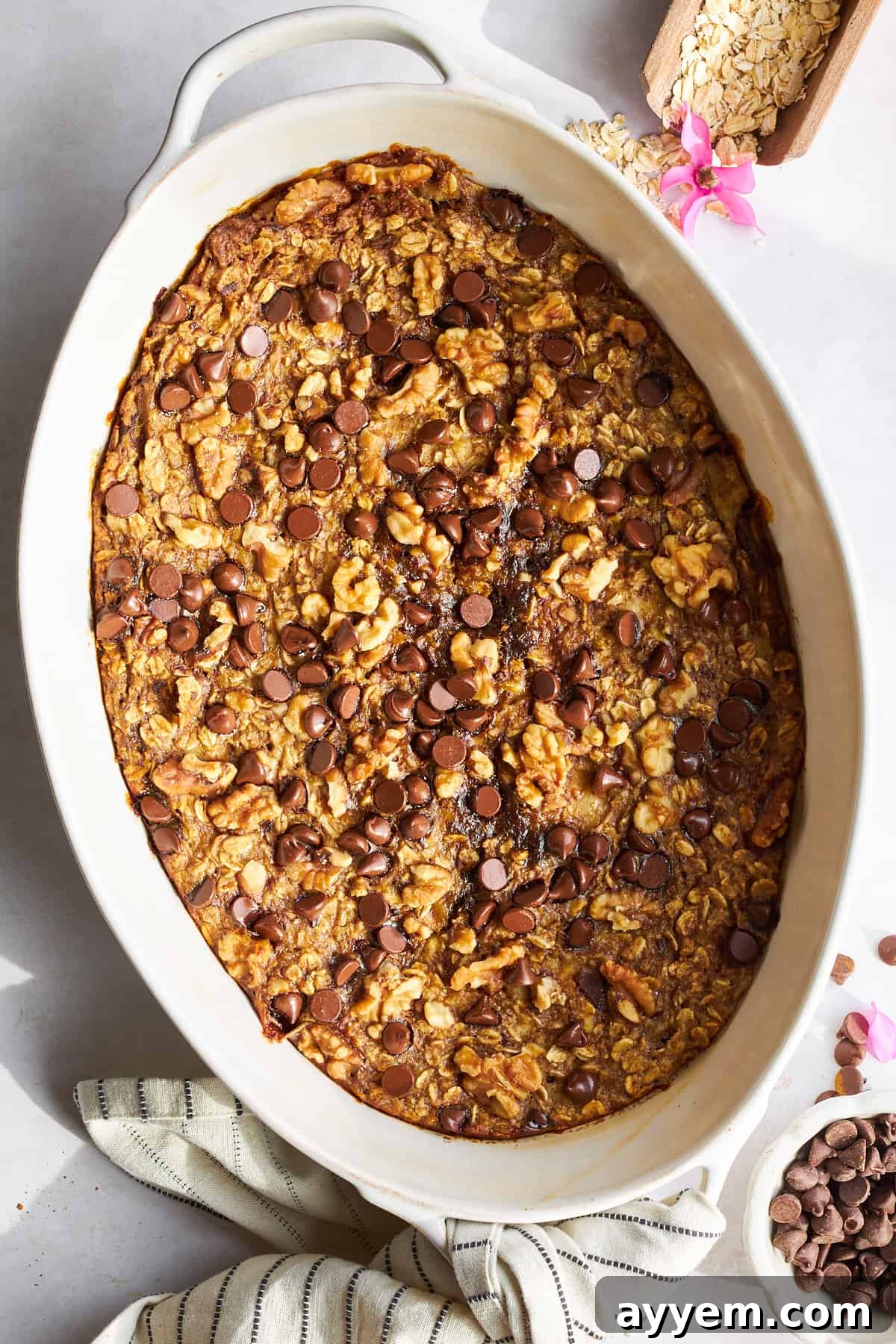 A large oval baking dish filled with golden-brown banana date baked oatmeal, generously topped with melted dark chocolate chips.