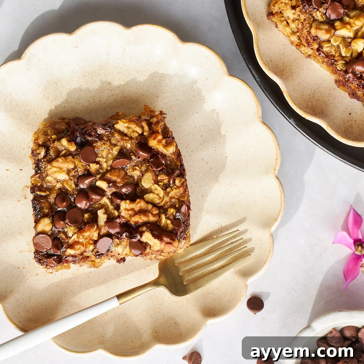 A square of banana date oatmeal on a plate with a fork, ready to be enjoyed.