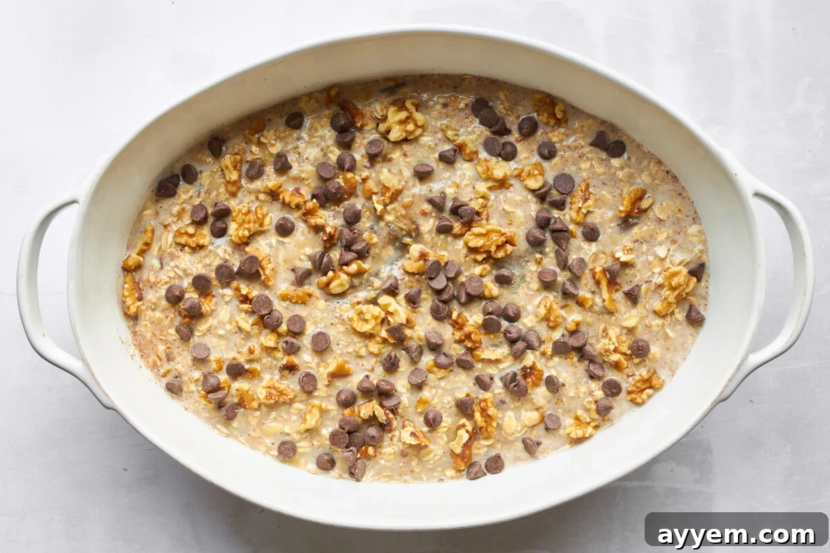 Unbaked banana date oatmeal mixture topped with chocolate chips in an oval baking dish.