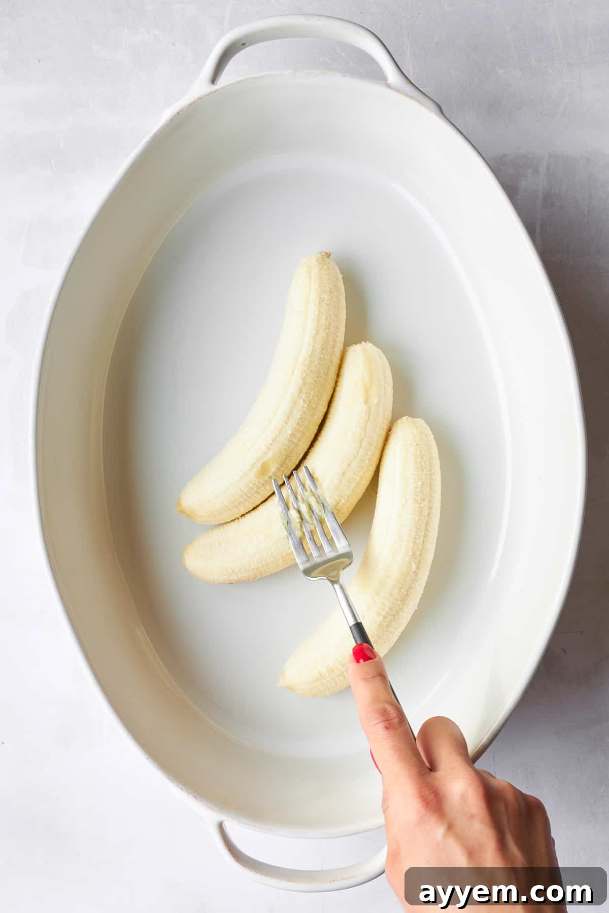 Three ripe bananas being mashed with a fork in a baking dish.