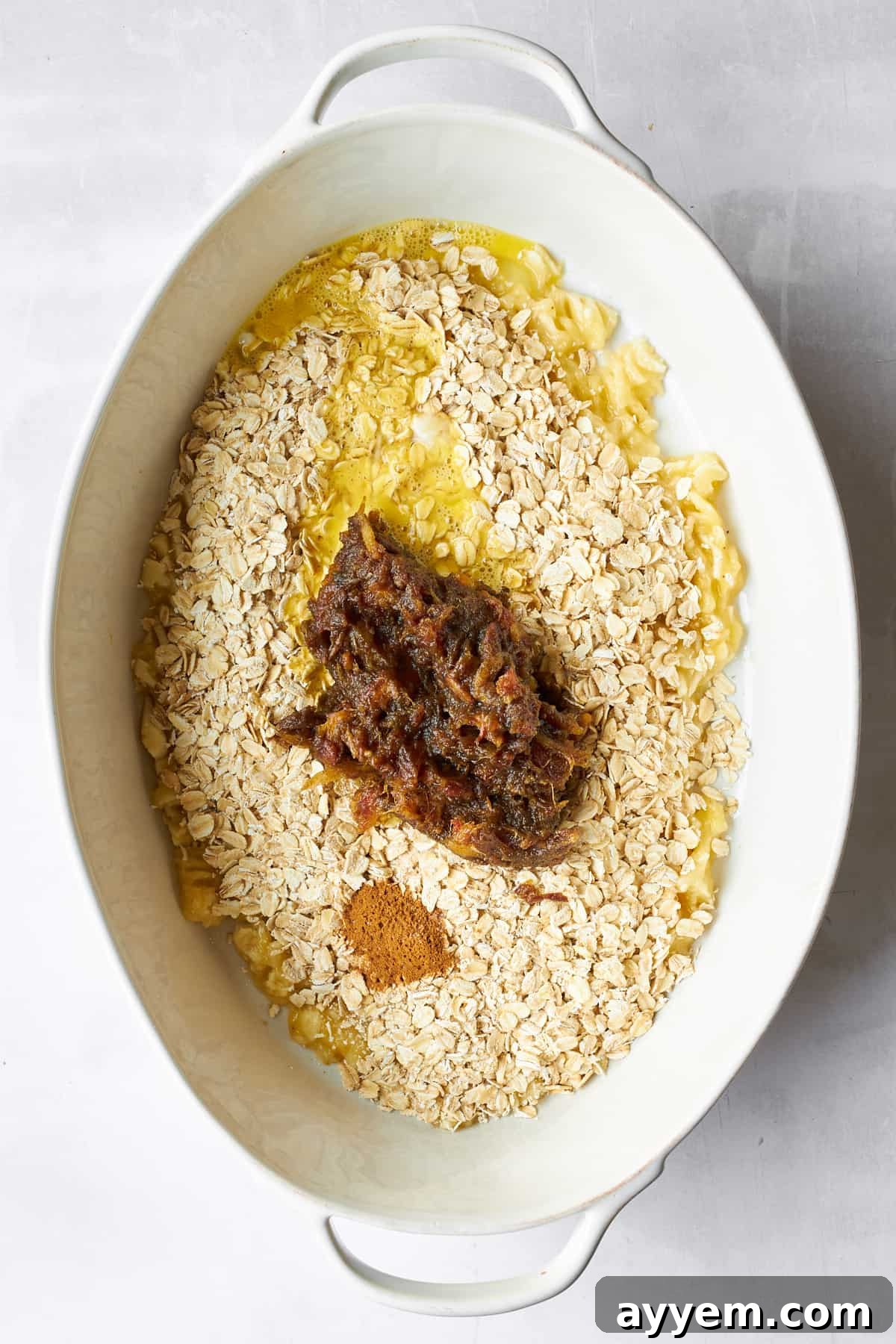 All dry and wet ingredients for banana date oatmeal gathered in an oval baking dish before mixing.