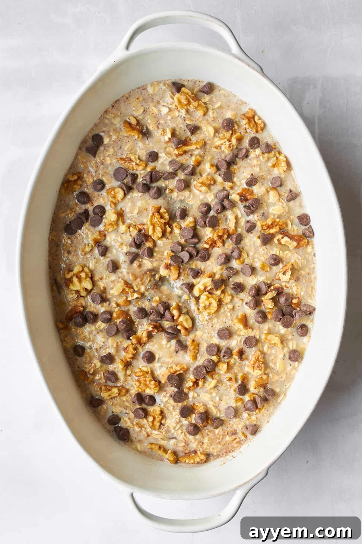 Uncooked banana date oatmeal mixture topped with chocolate chips in an oval baking dish, ready for the oven.