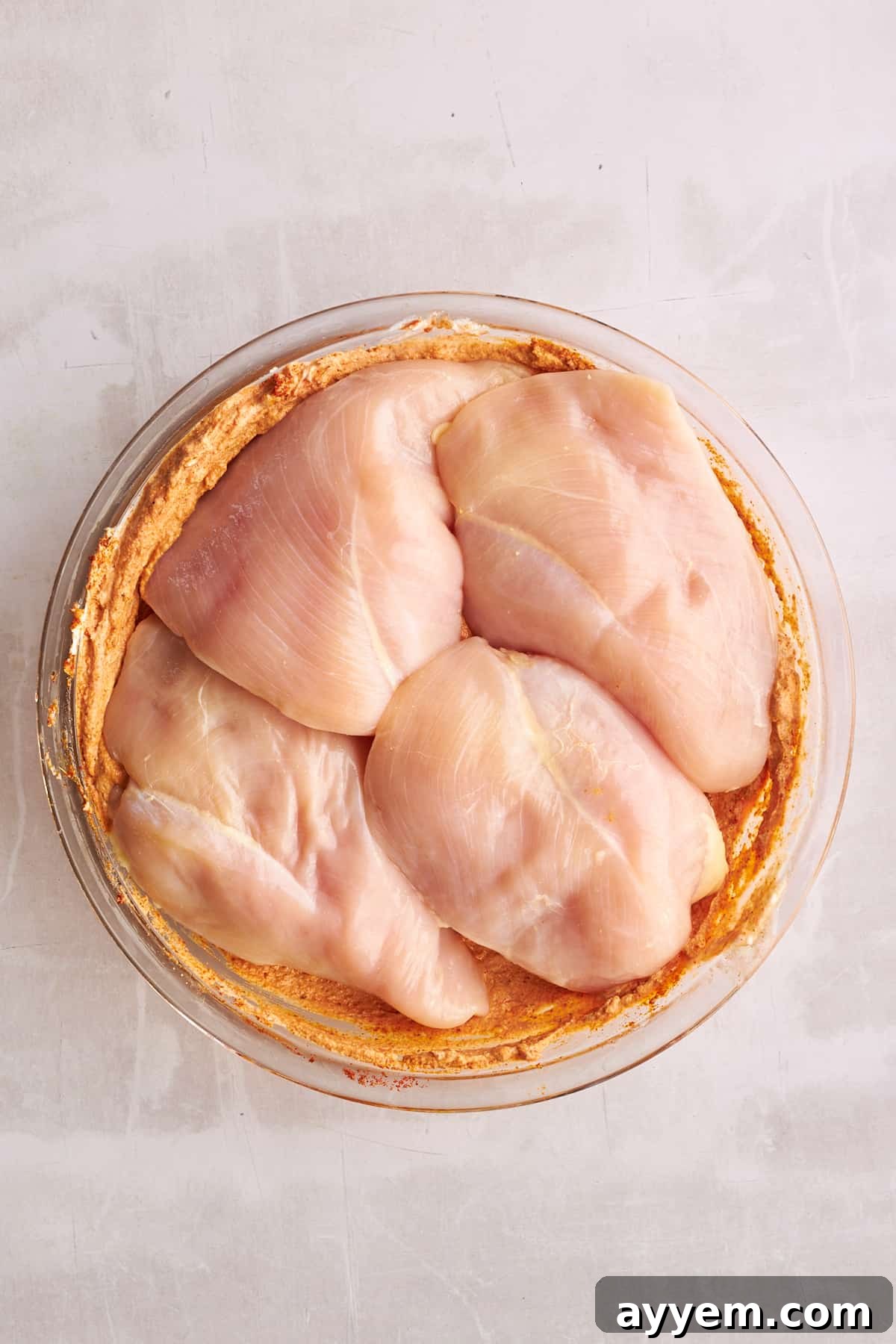 Raw chicken breasts in a bowl of shawarma marinade.