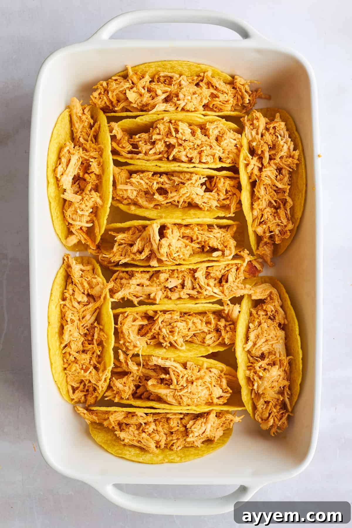 Shredded chicken shawarma stuffed in hard taco shells in a baking dish.