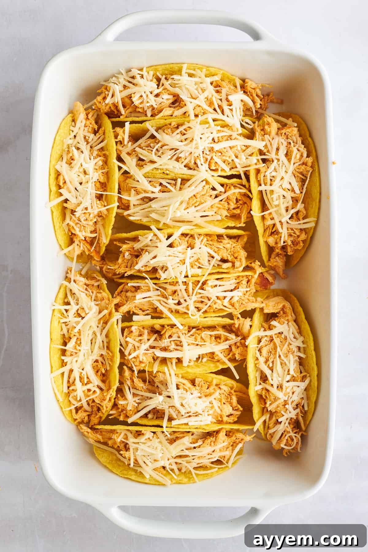 Hard shell tacos in a baking dish stuffed with shredded chicken shawarma and cheese.