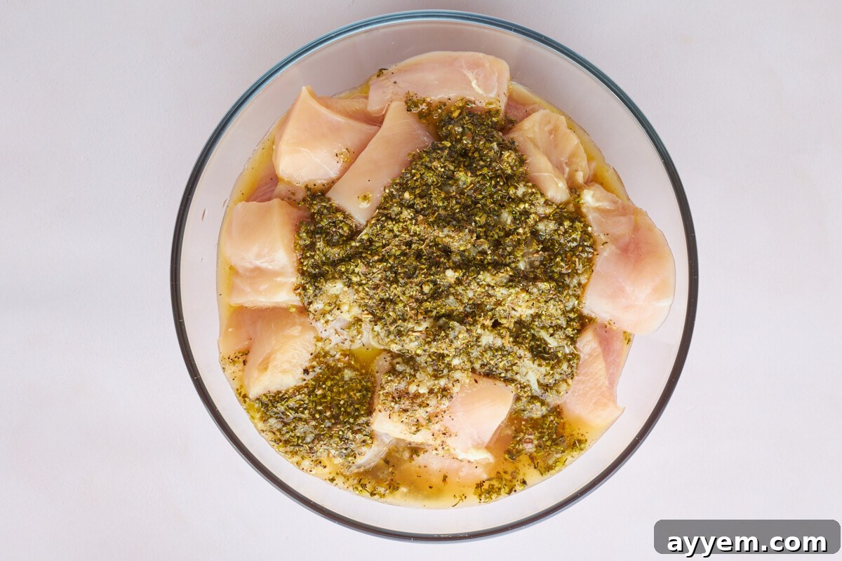 Raw chicken pieces marinading in a bowl of souvlaki marinade.