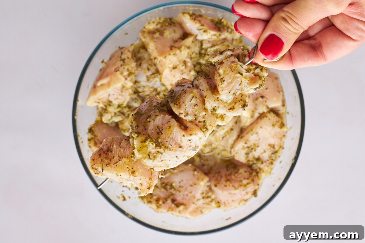 Raw marinaded souvlaki chicken being threaded on skewers.