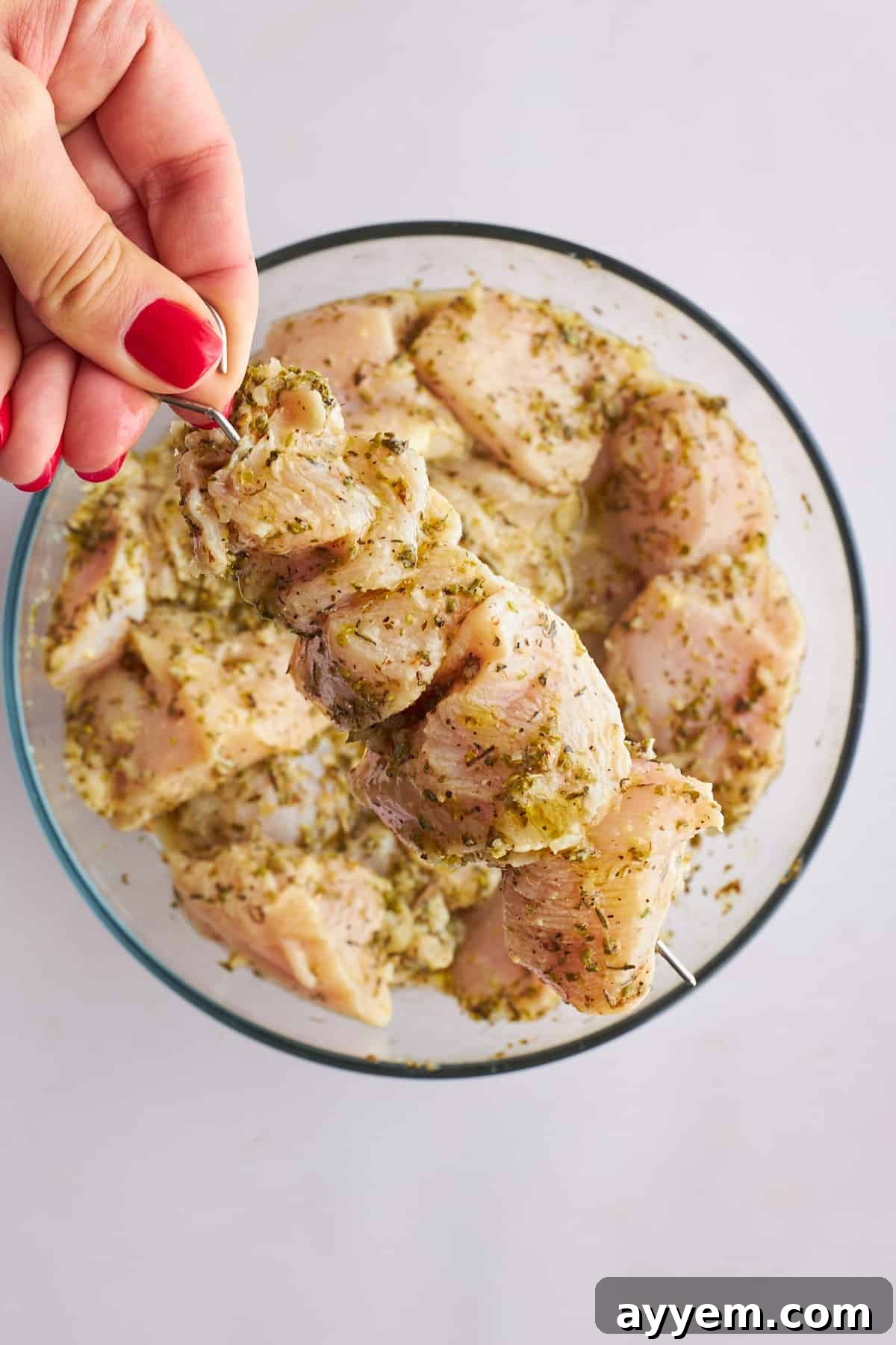 Raw chicken souvlaki being threaded onto skewers.