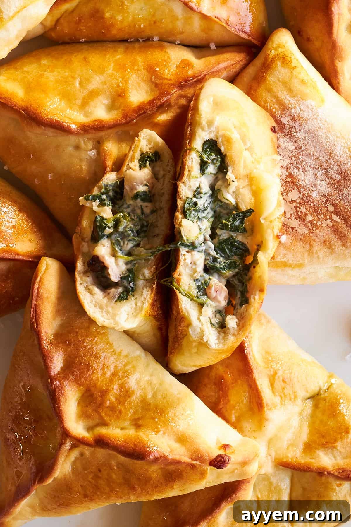 A close-up of baked spinach and cheese fatayer, with one perfectly split in half to reveal the warm, melty filling.