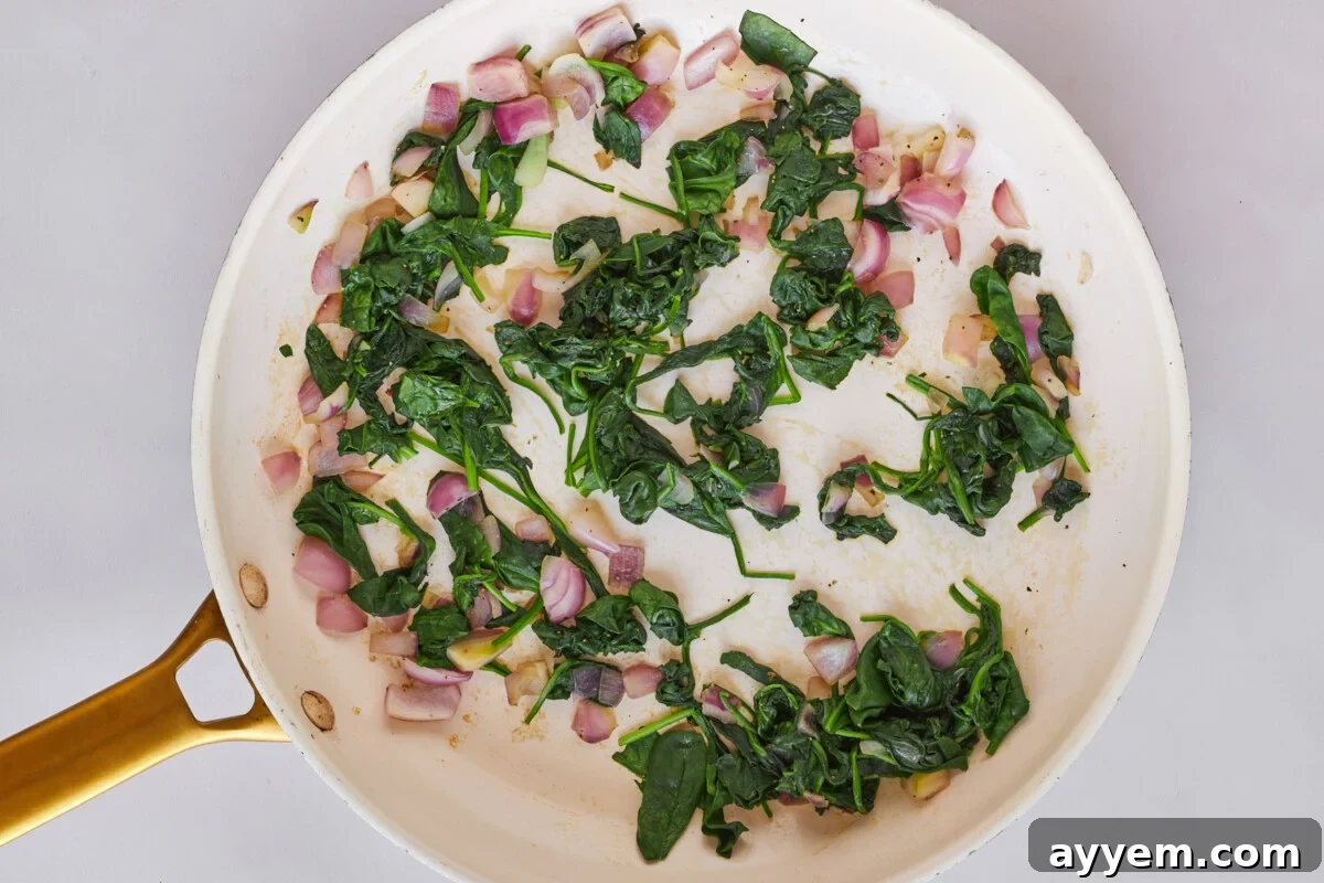Spinach and shallot being sautéed in a skillet.
