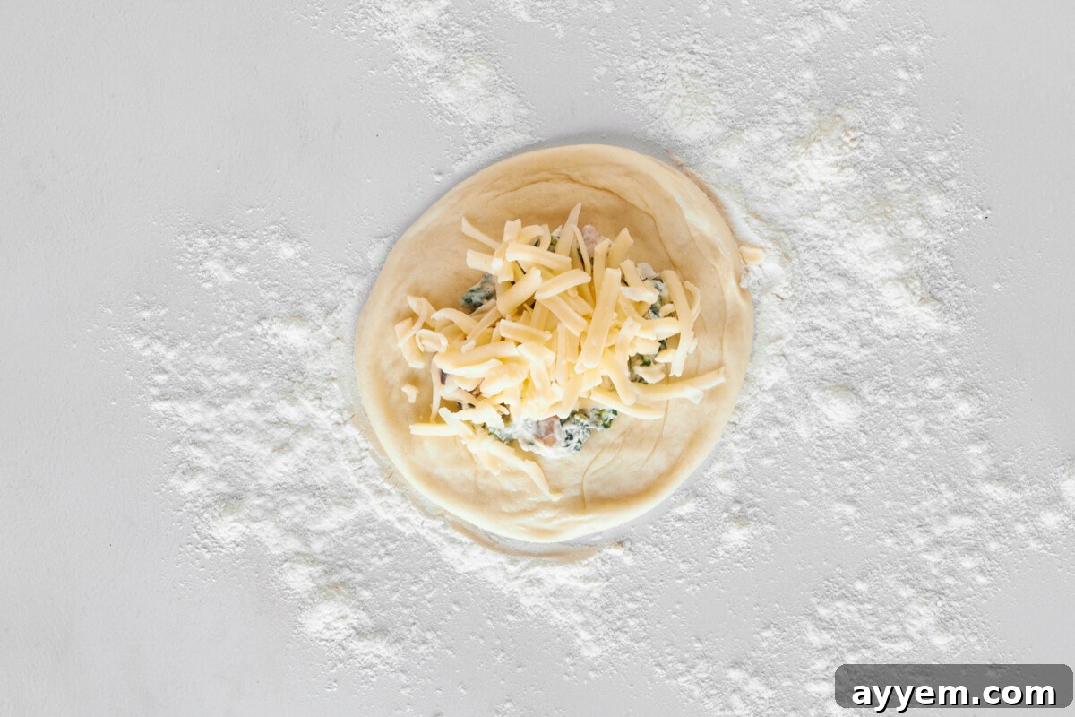 A dinner roll topped with a spinach and cheese mixture and shredded cheese.