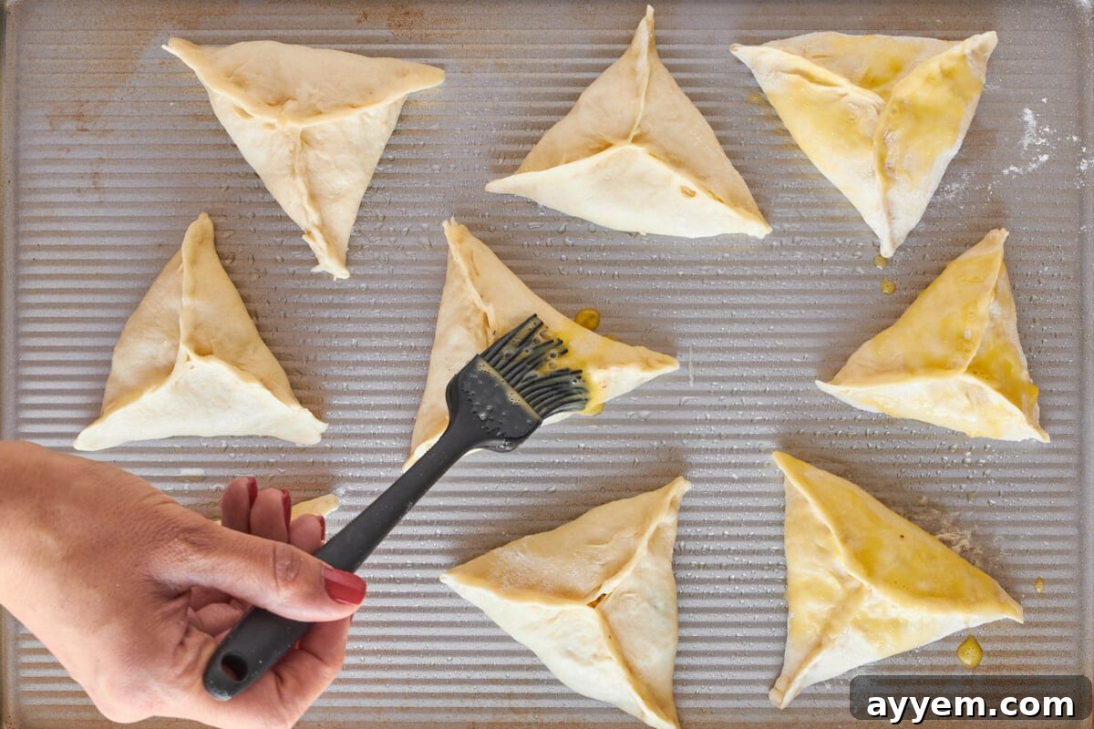 Fatayer on a baking sheet being brushed with egg wash.
