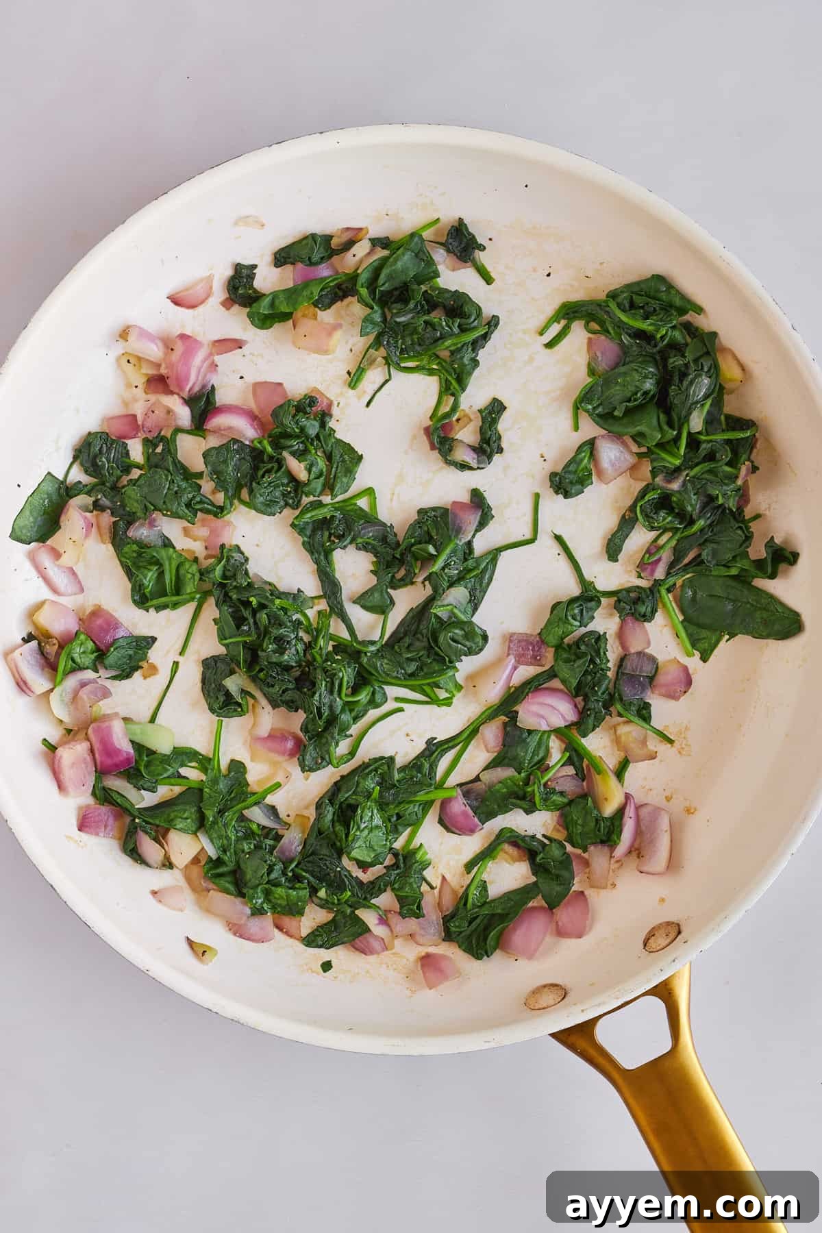 Wilted spinach and softened shallots cooling in a skillet after being perfectly sautéed.