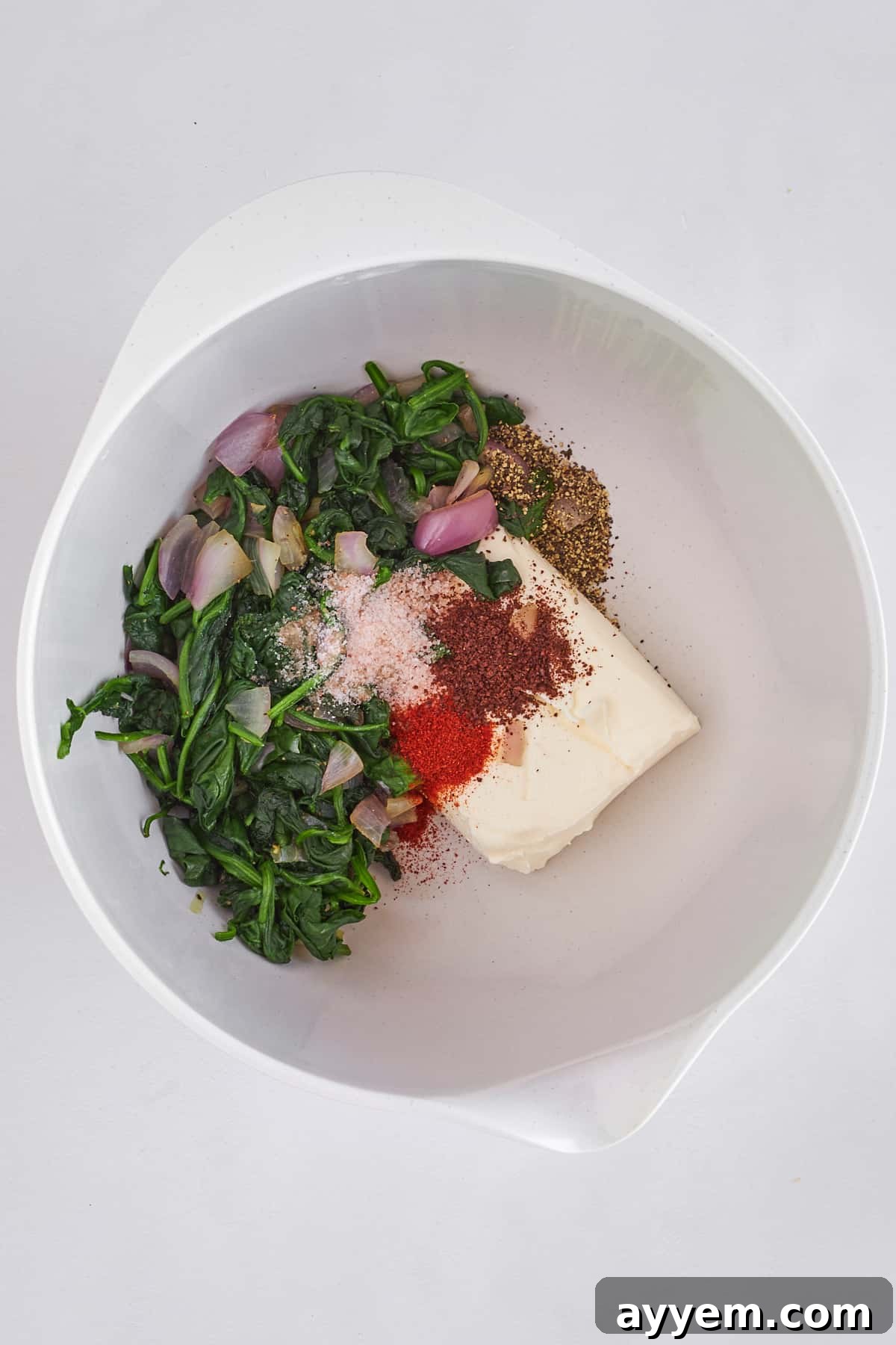 A delicious mixture of sautéed spinach, shallots, cream cheese, and spices being combined in a large bowl, forming the savory fatayer filling.